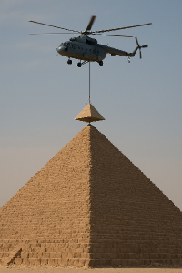 Pyramida a vrtulník co na laně veze a usazuje její špičku čili poslední horní díl vměřítku asi jedna desetina její výšky