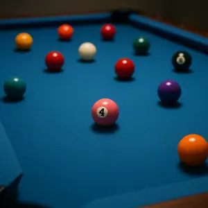 Detail kulečníkového stolu s modrým plátnem, na kterém se růžně nachází kulečníkové koule