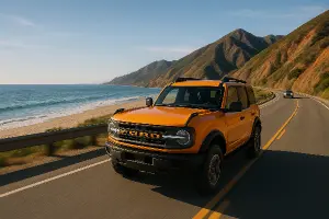 velky oranzovy ford na jedne strane cesty more a plaz a na druhe hory a na ceste auto