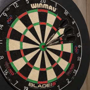 šipkový terč značky winmau blade 6 se třemi šipkami zapíchnutými v červeném středu. Vzhled šipek kovové hroty a tělo