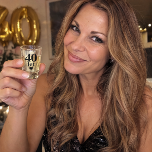 žena, dlouhe vlasy, tmavší blond, drří skelníčku s nápisem 40 let