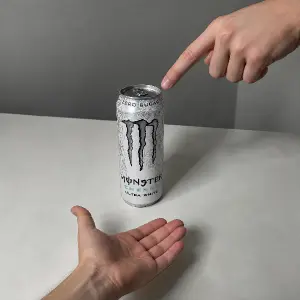 Monster ultra white s normální lidskou rukou co na nej z výšky z boku ukazuje a pod nim ruka venom