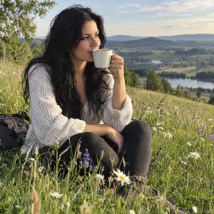 černovlasá žena sedící na louce a pije kávu