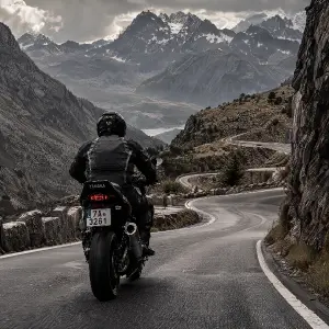 motorkář zezadu, motorka Yamaha, před ním klikatá cesta, okolo hory, černobílý styl, může být šedá, hnědá